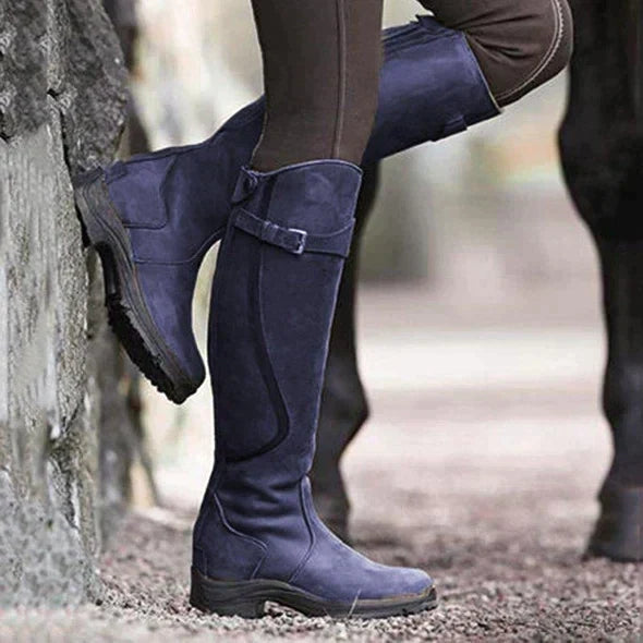 Une paire de bottes violettes, hauteur genou, pour femmes, avec un détail de boucle sur le côté et une semelle en caoutchouc durable, idéales pour l'hiver et les activités en plein air.