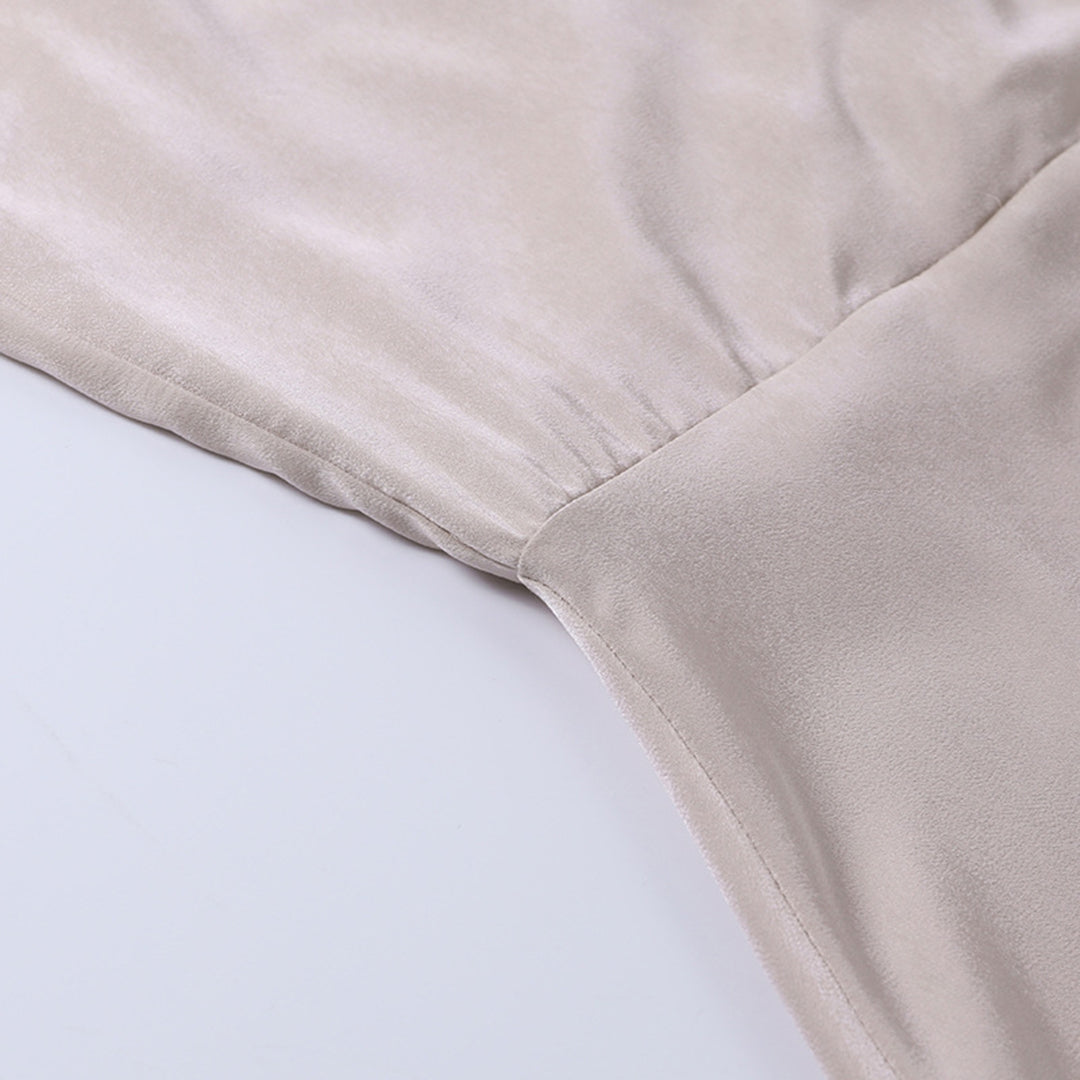 Vue rapprochée du tissu satiné d'une robe longue fluide pour femme, mettant en avant la couture soignée et la texture douce et légèrement brillante du matériau beige clair. L’image illustre la qualité et la finition élégante du vêtement, idéale pour un style raffiné et féminin.