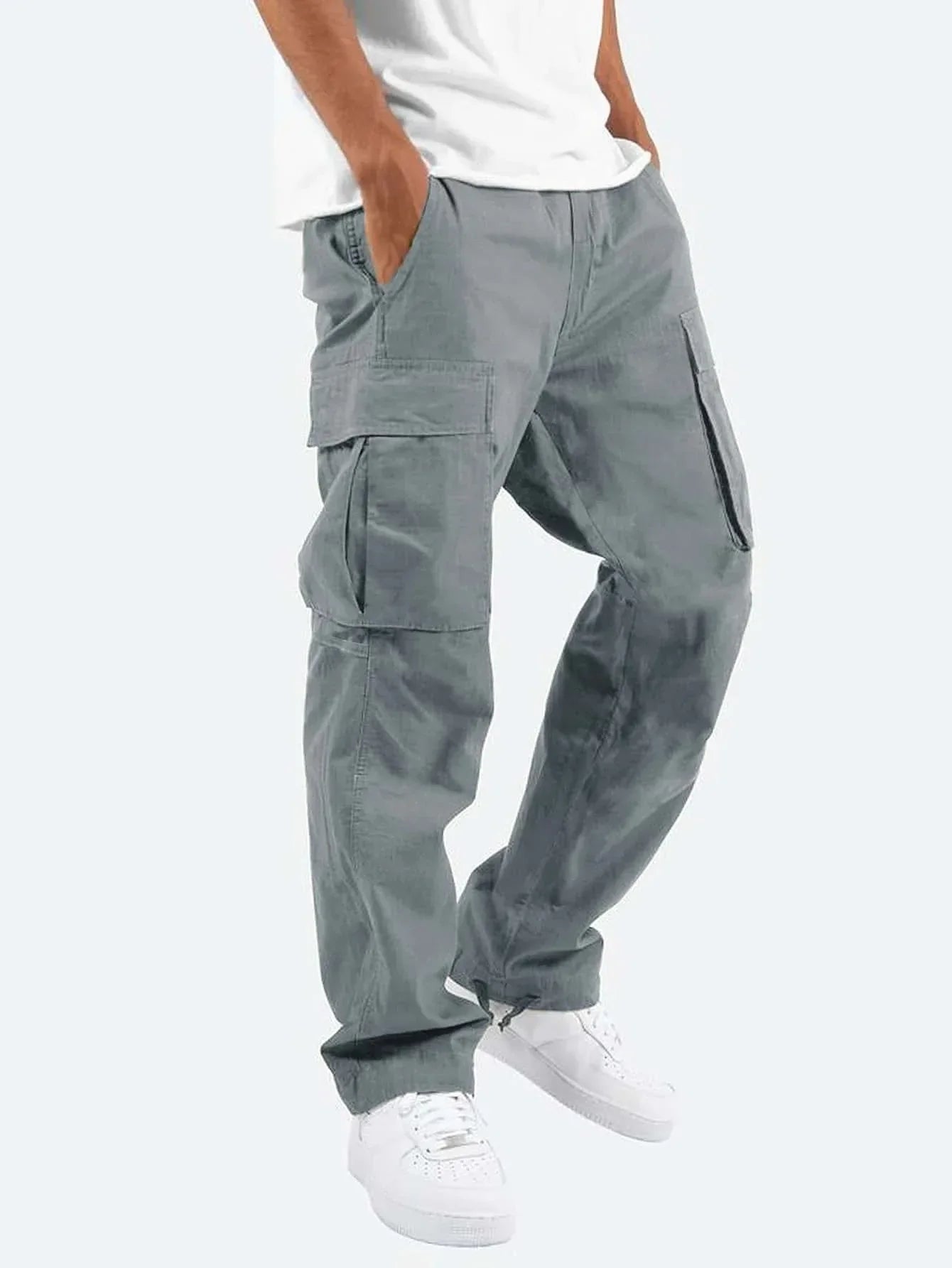 Pantalon droit homme Arsène tendance style cargo en coton gris, avec grandes poches latérales, porté avec un t-shirt blanc et des baskets blanches, sur fond clair.