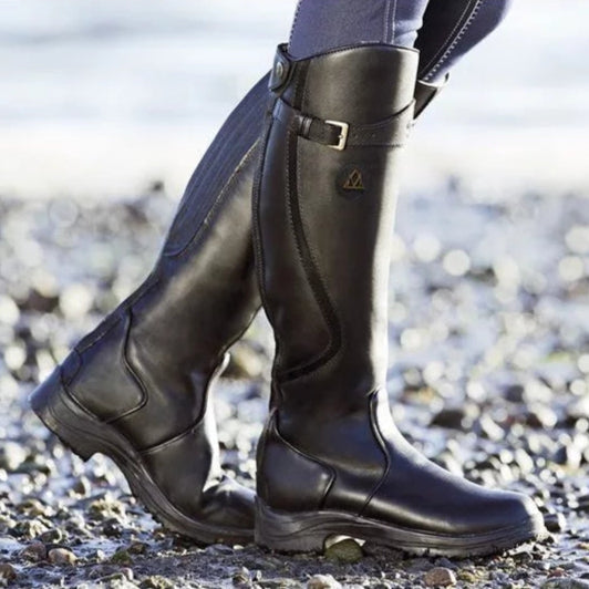 Un gros plan de bottes en cuir noir, hauteur genou, avec un détail de boucle sur le côté, conçues pour la durabilité et le confort, parfaites pour les conditions hivernales et les activités en plein air.