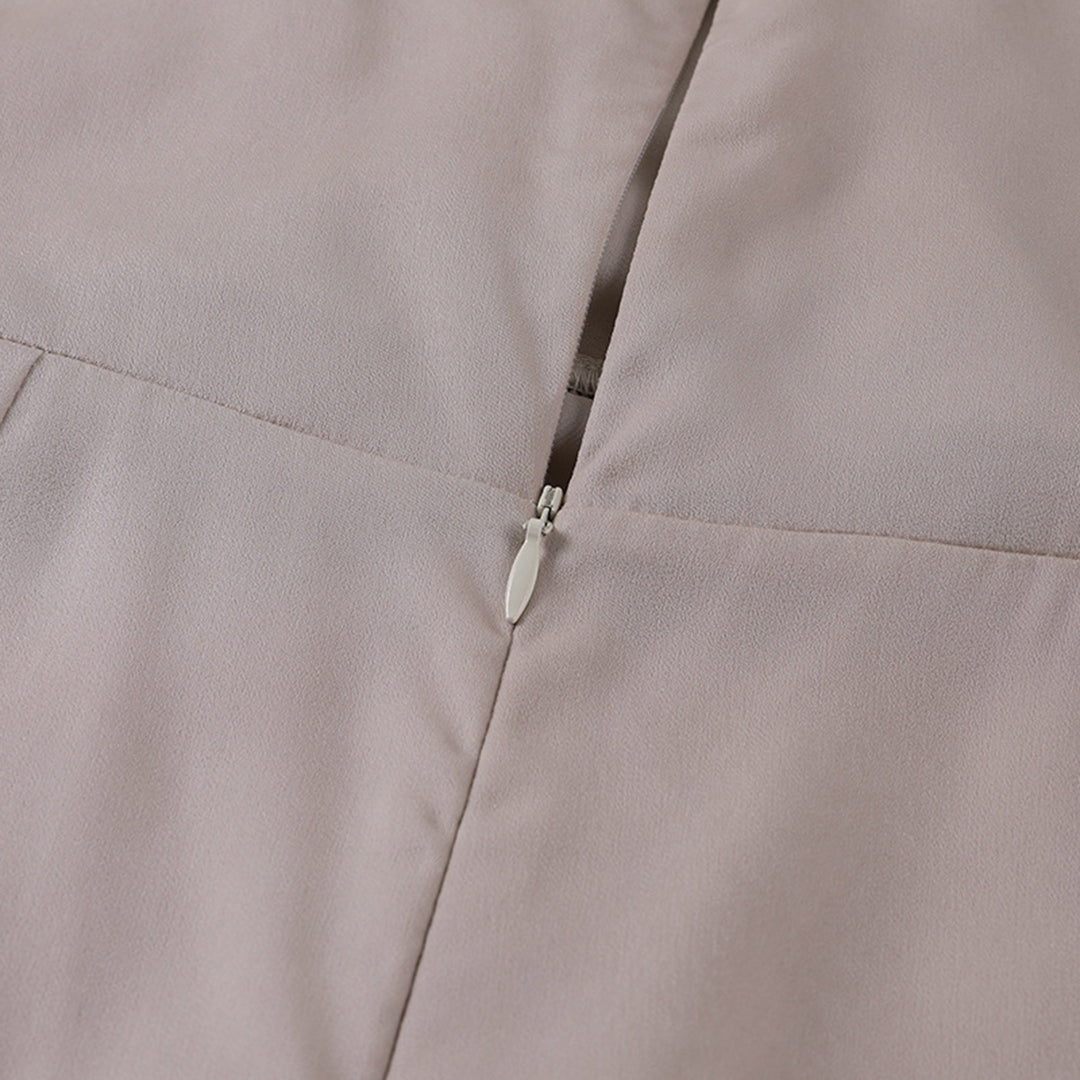 Vue rapprochée d’une fermeture éclair argentée sur une robe en satin beige clair. L’image met en valeur la texture fluide et élégante du tissu ainsi que la finition soignée de la couture, illustrant la qualité et le raffinement du vêtement.